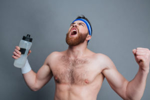 58469565 - furious bearded young sportsman with bottle of water standing and shouting over grey background